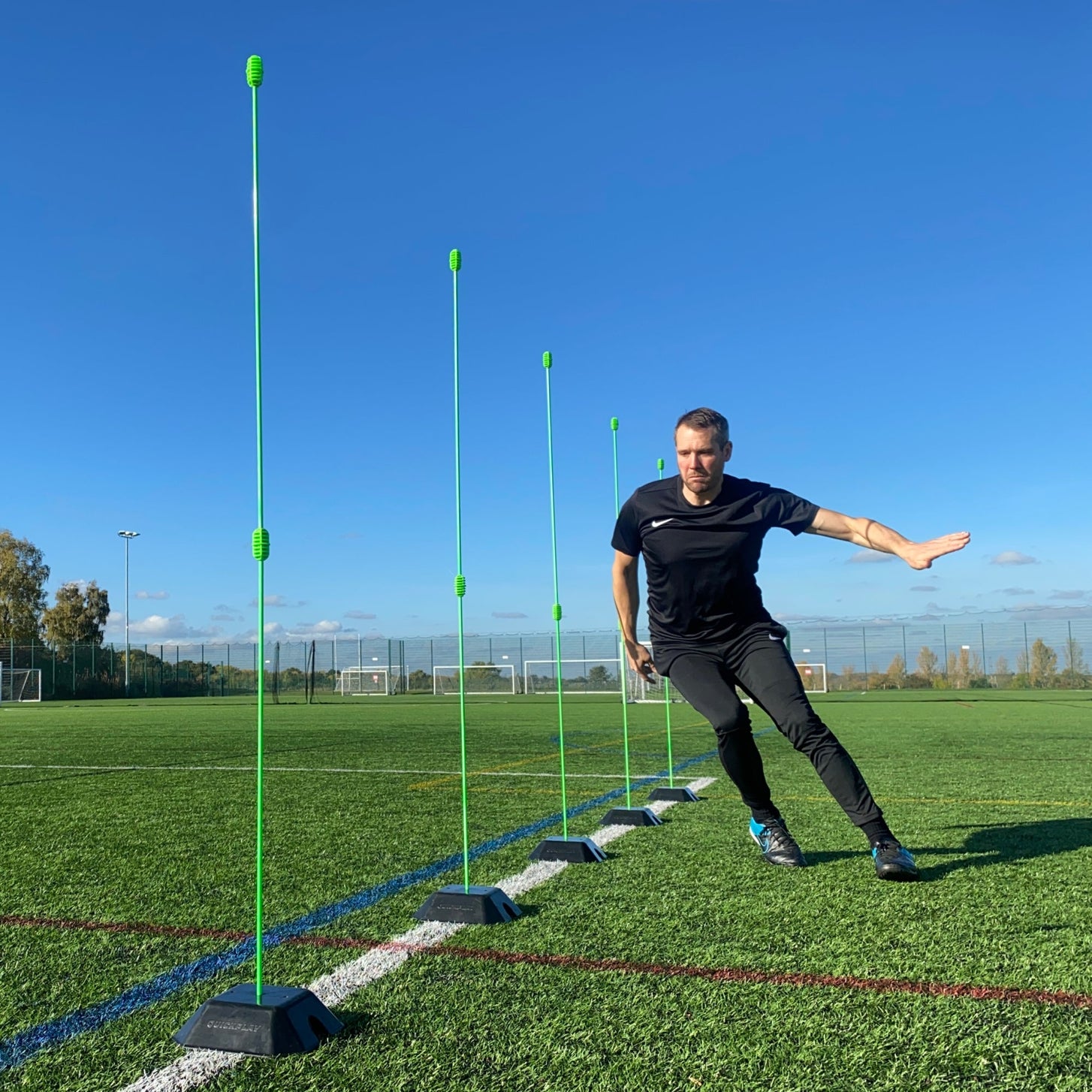 Basisgewicht 2er-Set für KICKSTER, SPOT und Slalomstangen: Spieler läuft durch eine Reihe grüner Stangen in schwarzen Gewichten auf einem Platz.