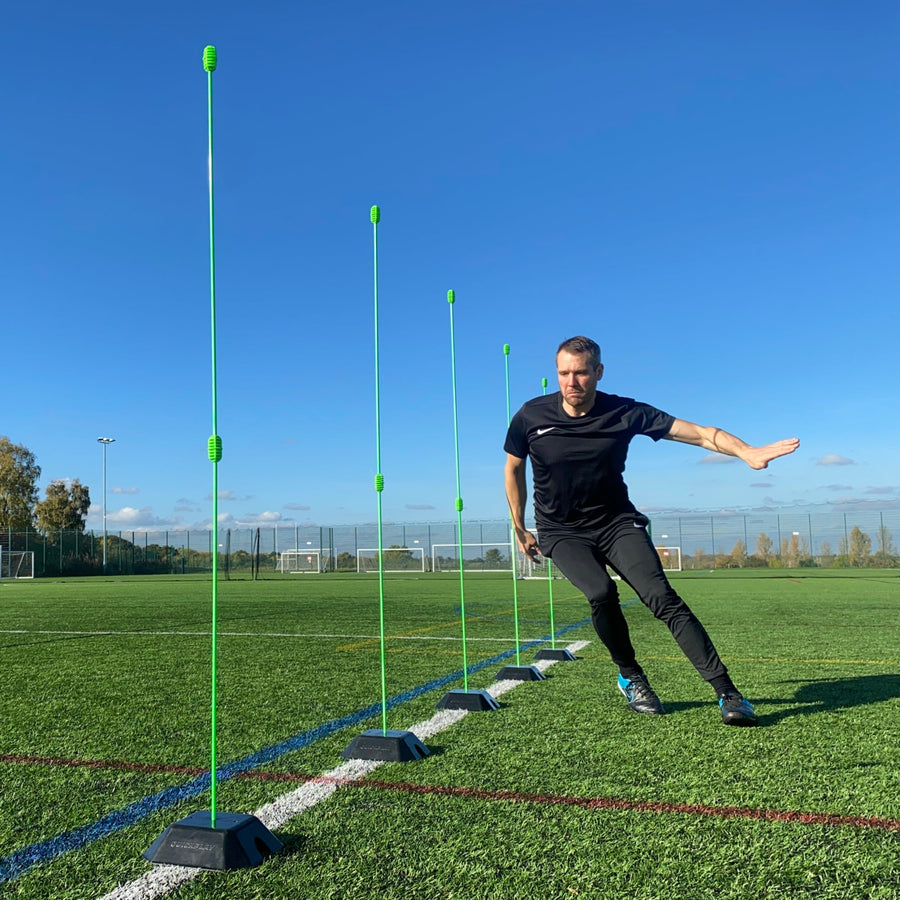 Basisgewicht 2er-Set für KICKSTER, SPOT und Slalomstangen: Spieler läuft durch eine Reihe grüner Stangen in schwarzen Gewichten auf einem Platz.