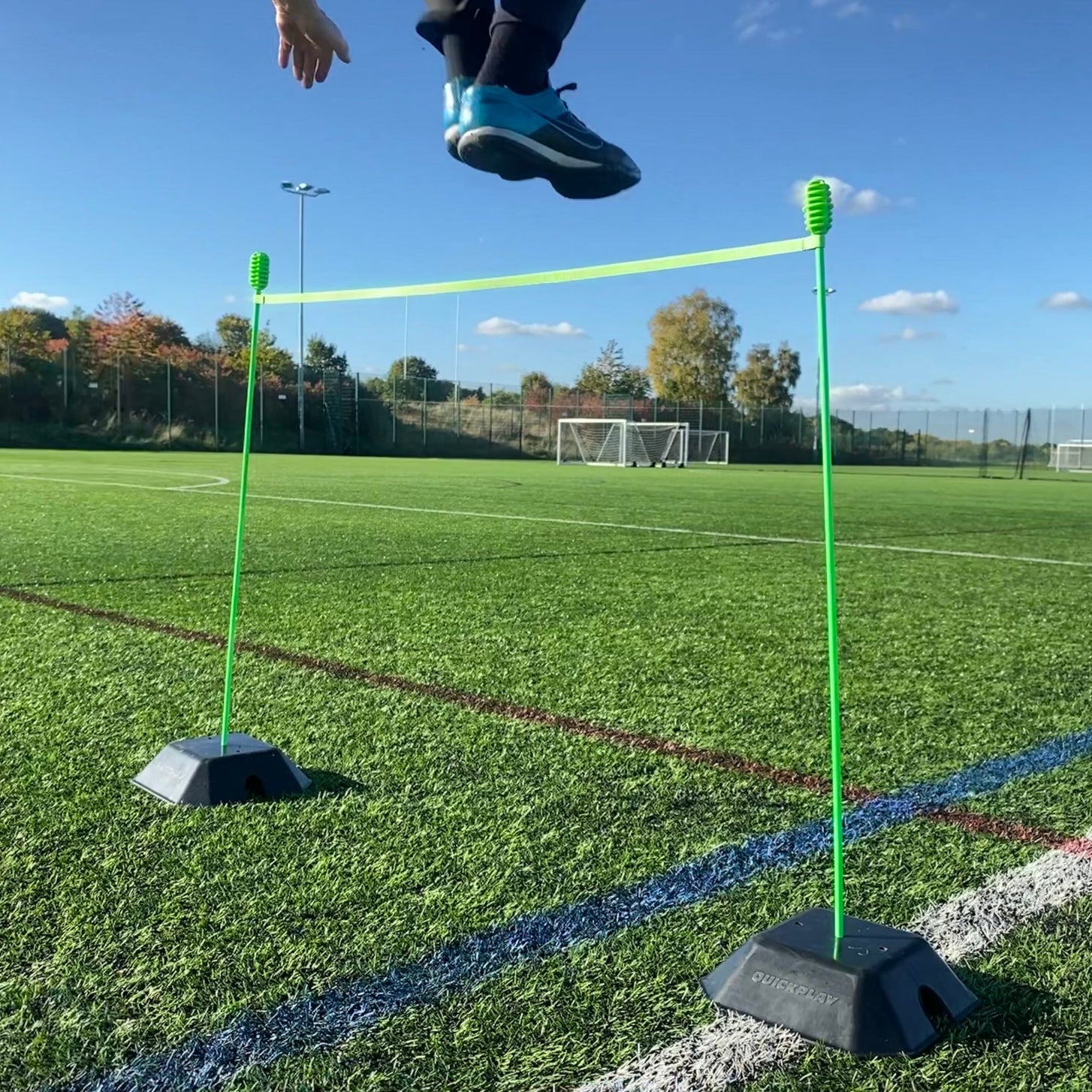 Basisgewicht 2er-Set für KICKSTER, SPOT und Slalomstangen: zwei Gewichte halten grüne Stangen und eine Querstange als Hürde, ein Spieler springt darüber.
