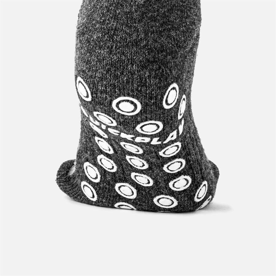 Sohle einer dunkelgrauen QUICKPLAY Grip-Socke in Nahaufnahme, mit weißen ringförmigen Grip-Noppen und QUICKPLAY Logo.