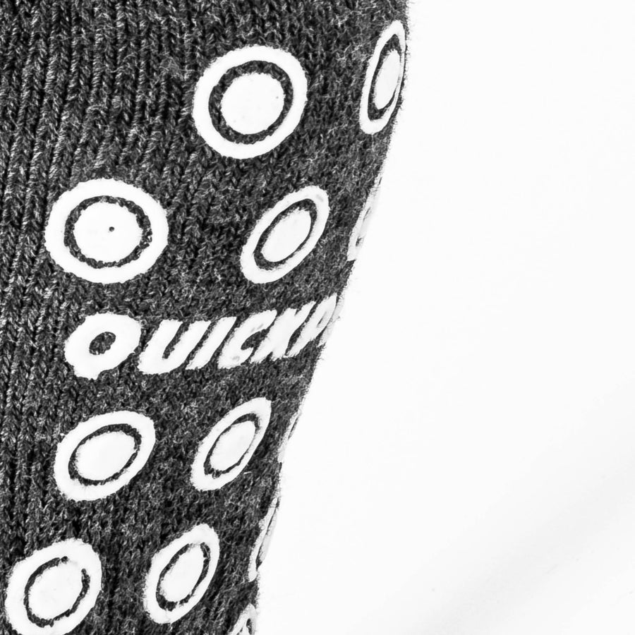 Nahaufnahme der weißen QUICKPLAY Grip-Noppen und des Logos auf der dunkelgrauen Strick-Sohle einer Grip-Socke.