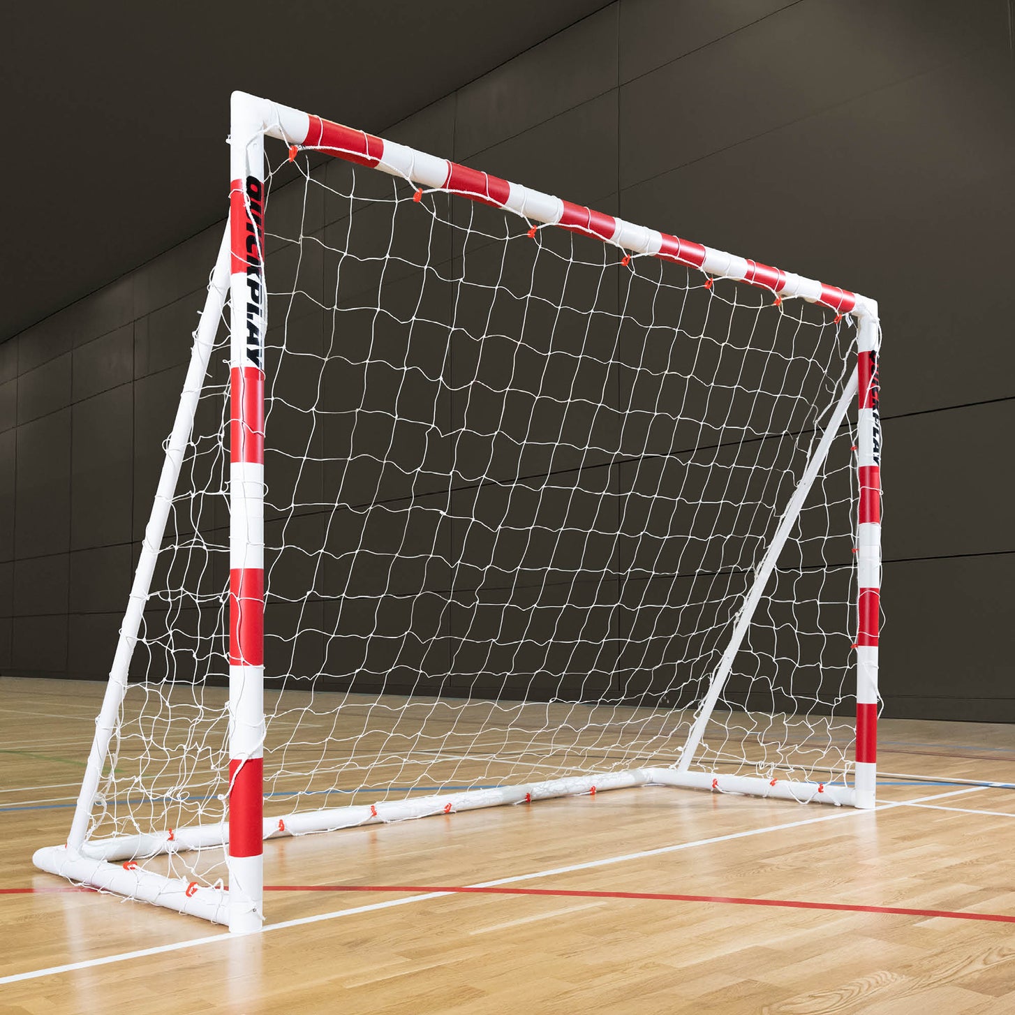 Q-FOLD Klappbares Handballtor 300 x 200 cm mit rot-weiß gestreiften Pfosten und weißem Netz, auf dem Holzboden einer Sporthalle.