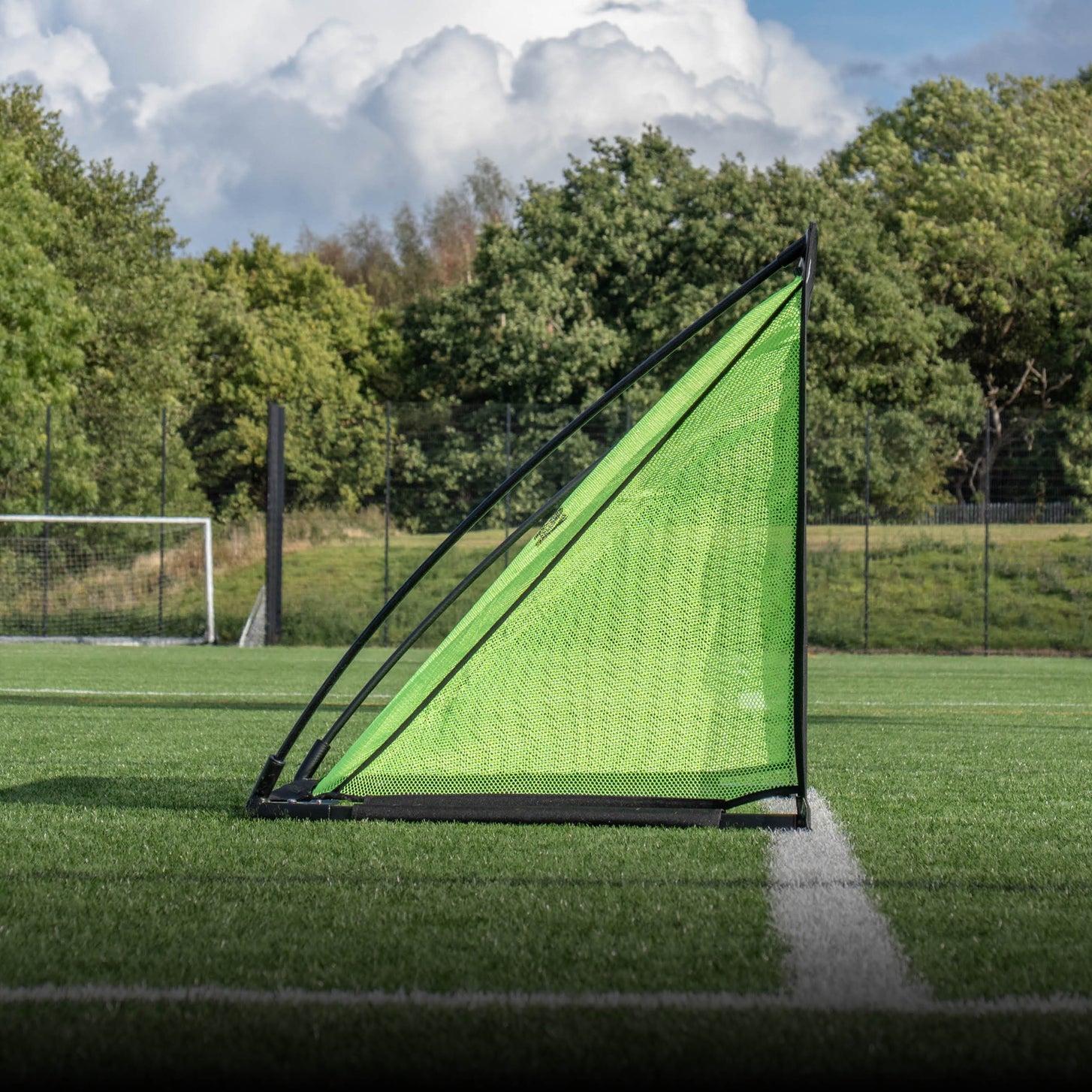KICKSTER PRO Tor 150 x 100 cm von der Seite mit schräg abfallendem grünem Netz, auf einem Kunstrasenplatz mit Bäumen dahinter.