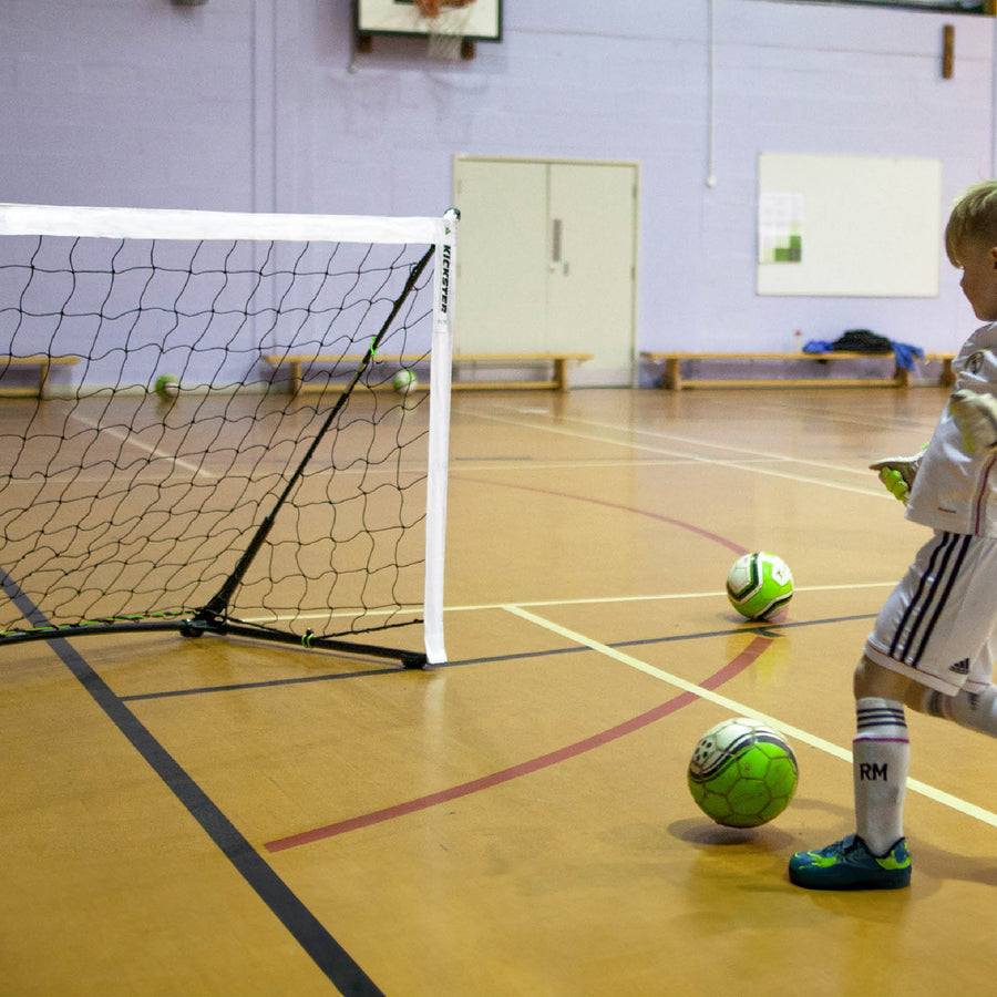 Kind schießt gleich einen Ball auf ein KICKSTER Tor auf dem Boden einer Sporthalle.