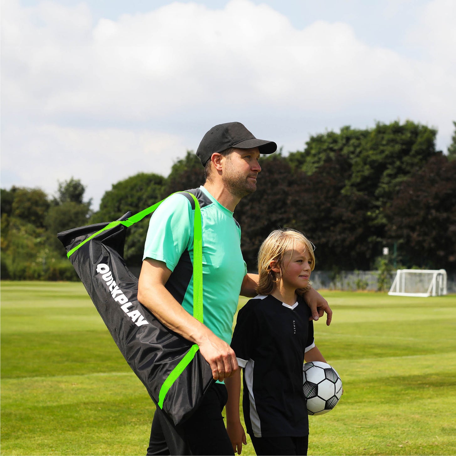 Tasche des KICKSTER Elite Tors 500 x 200 cm, getragen von einem Mann mit Kappe, der mit einem Mädchen mit Fußball über Rasen geht.