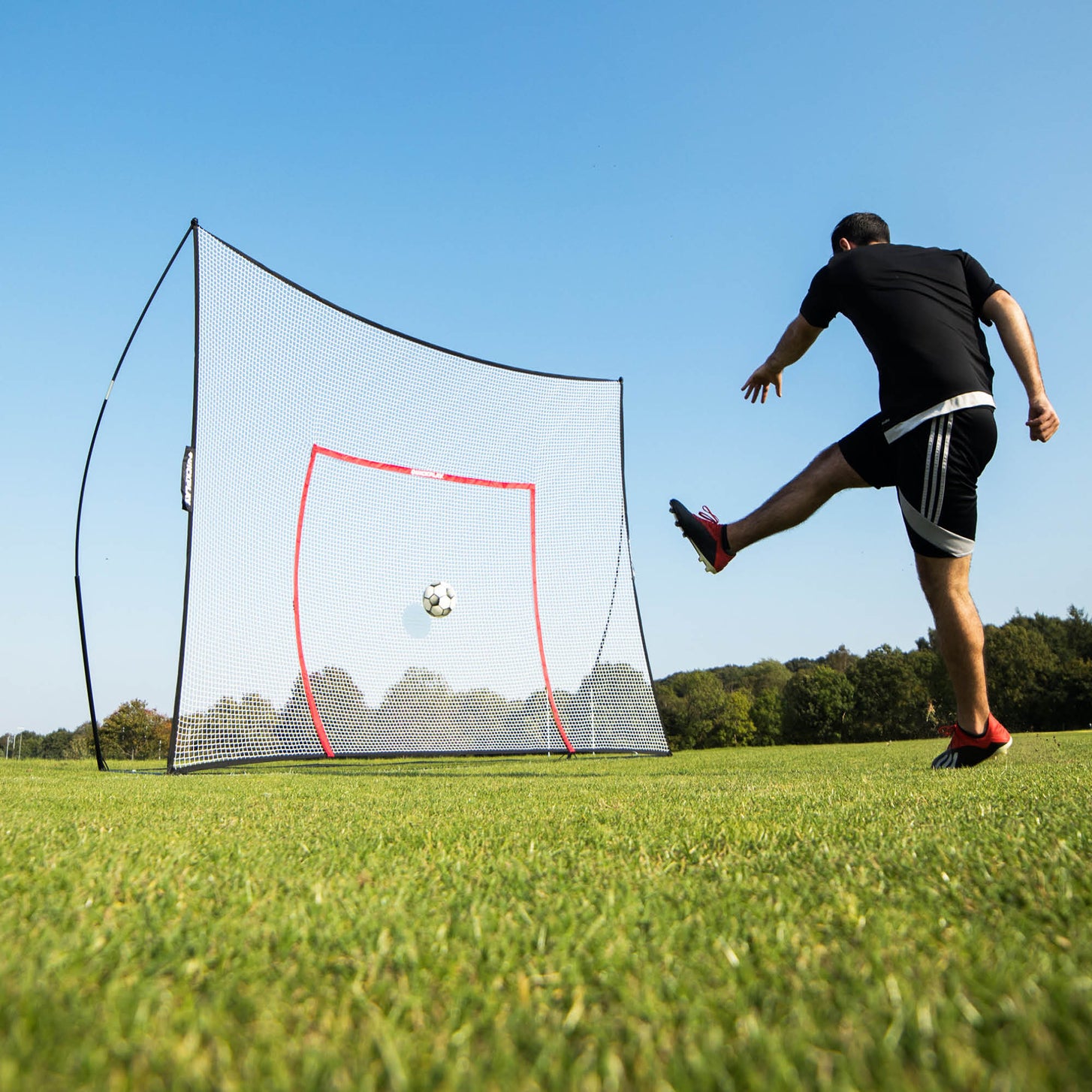 Spieler schießt einen Ball ins MEGA NET 370 x 270 cm auf Rasen, der Ball fliegt auf den orangefarbenen Zielrahmen zu.