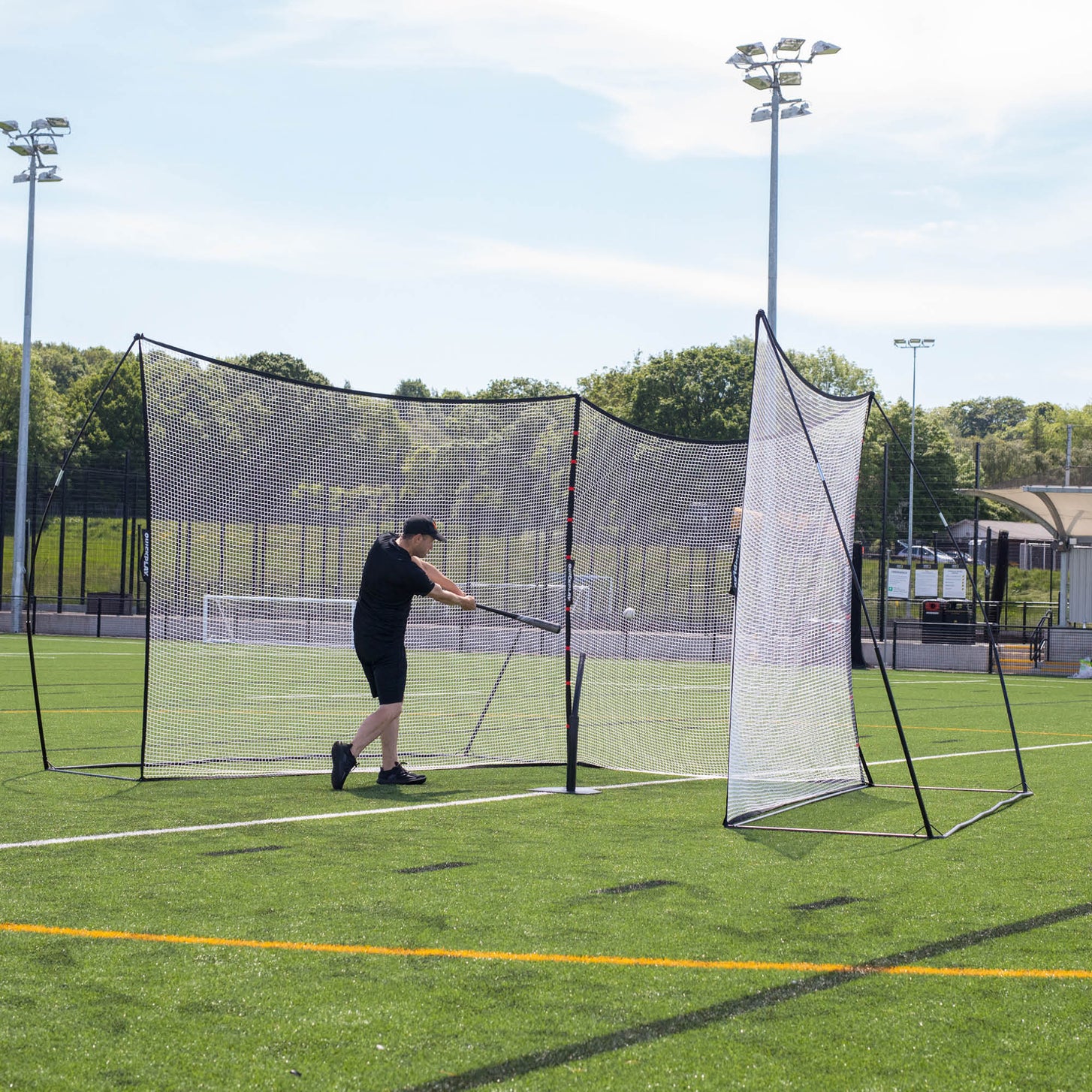 MEGA NET Ballfangnetze 370 x 270 cm auf einem Kunstrasenplatz, ein Spieler schlägt einen Baseball mit dem Schläger in die Netze.