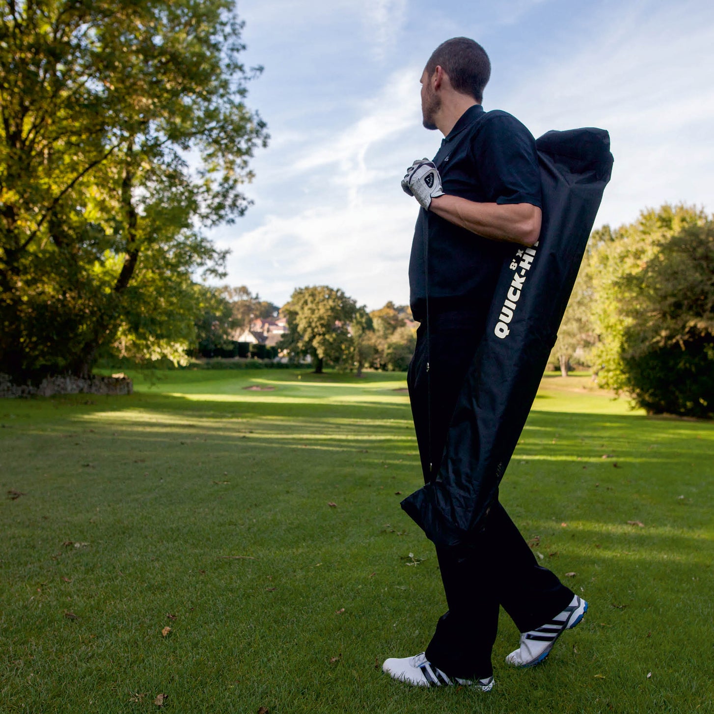 Golfer trägt das QUICK-HIT Golfnetz, verpackt in seiner schwarzen QUICK-HIT Tasche, über der Schulter auf einem Golfplatz.