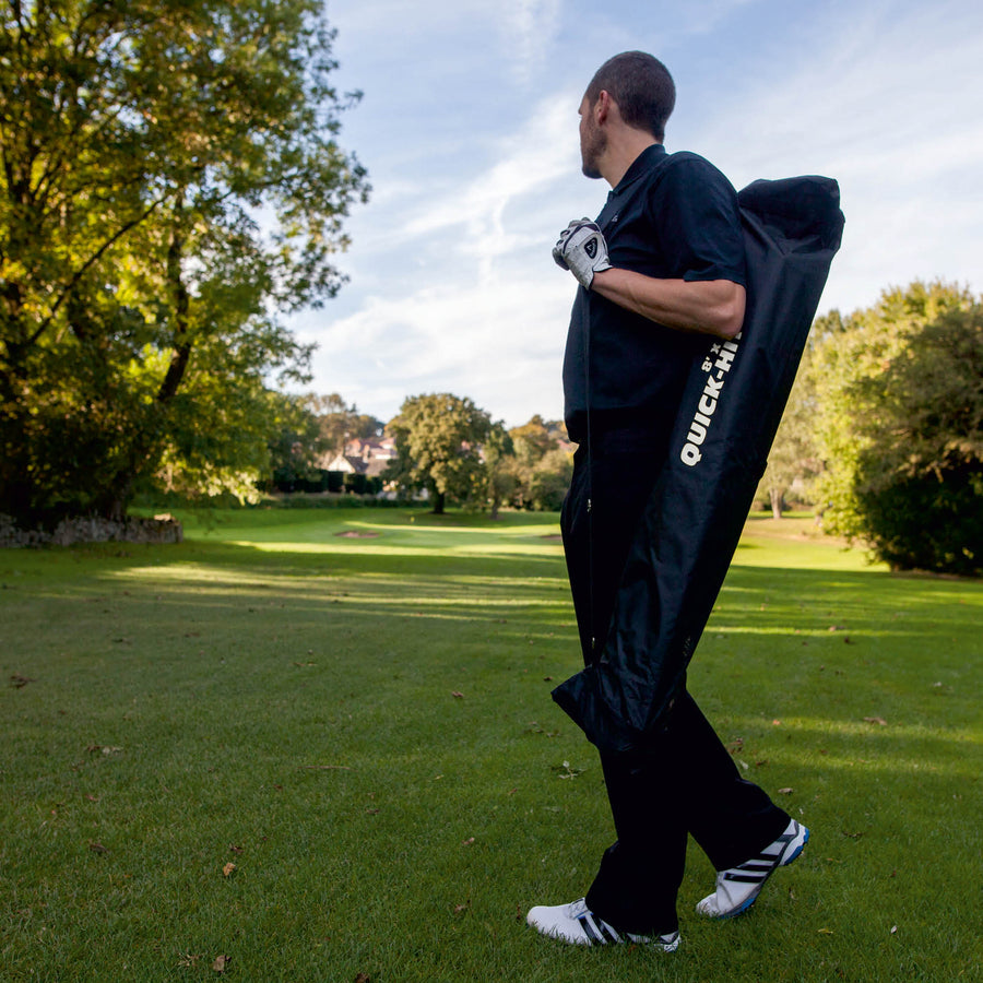 Golfer trägt das QUICK-HIT Golfnetz, verpackt in seiner schwarzen QUICK-HIT Tasche, über der Schulter auf einem Golfplatz.