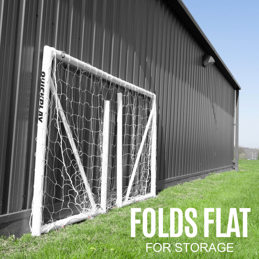 Q-FOLD Fußballtor 240 x 150 cm zusammengeklappt an ein dunkles Metallgebäude gelehnt, Text „folds flat for storage“.