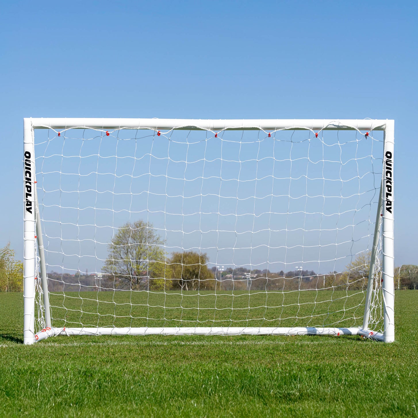 Q-FOLD Fußballtor 240 x 150 cm von vorn auf einem Rasenfeld, durch das weiße Netz sind Bäume zu sehen.