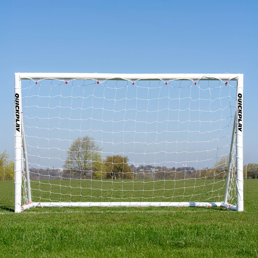 Q-FOLD Fußballtor 240 x 150 cm von vorn auf einem Rasenfeld, durch das weiße Netz sind Bäume zu sehen.