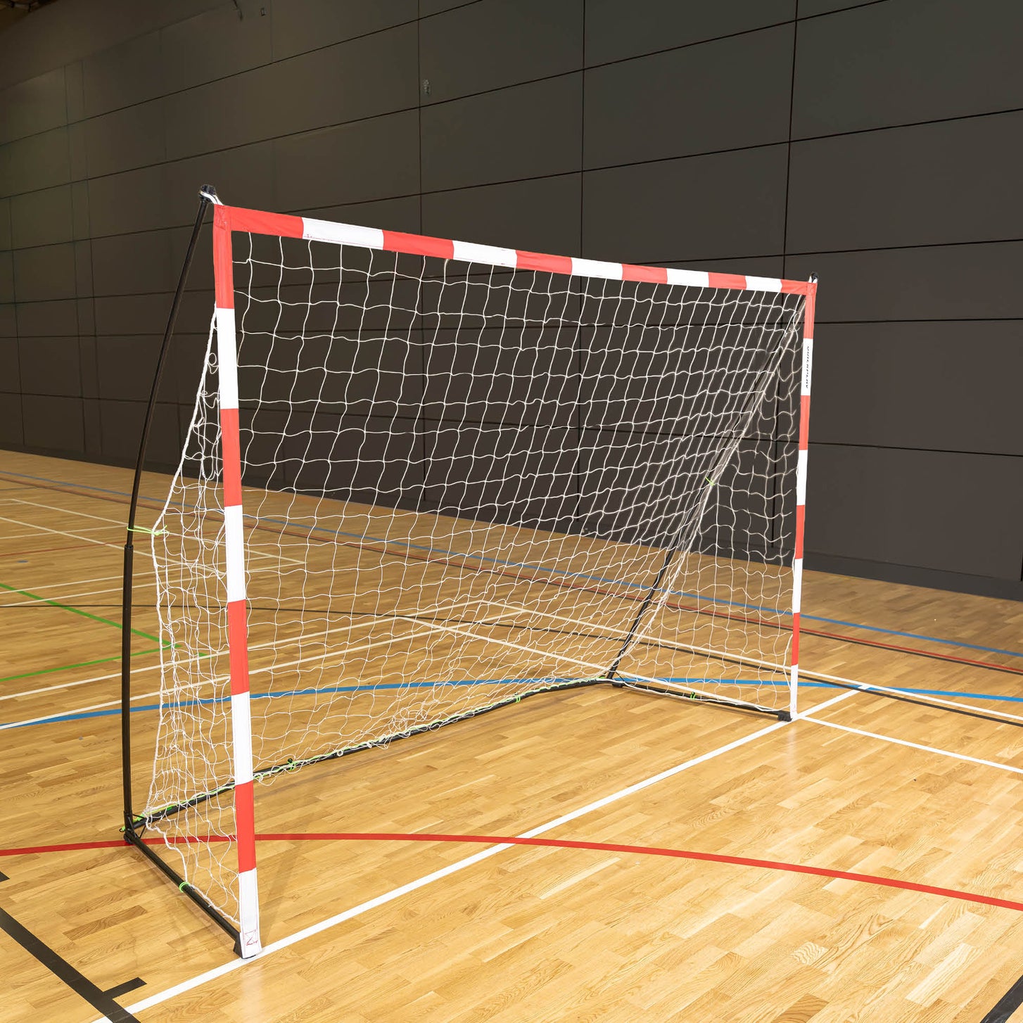 Tragbares Handballtor für Erwachsene 300 x 200 cm mit rot-weißem Rahmen und weißem Netz, auf dem Holzboden einer Sporthalle.