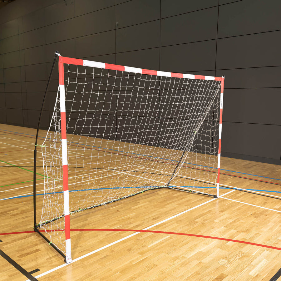 Tragbares Handballtor für Erwachsene 300 x 200 cm mit rot-weißem Rahmen und weißem Netz, auf dem Holzboden einer Sporthalle.