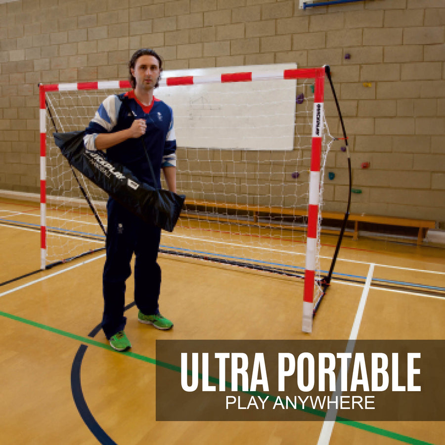 Mann hält eine schwarze QUICKPLAY Tasche vor dem tragbaren Jugend-Handballtor 240 x 170 cm in einer Sporthalle, Text „ultra portable“.