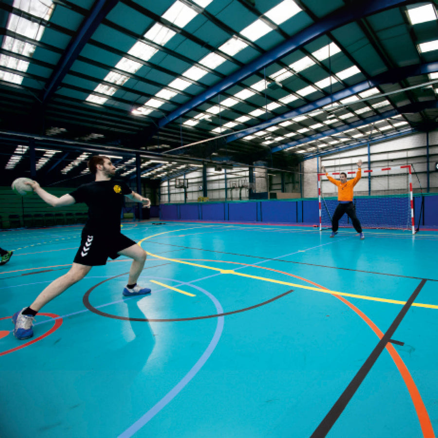 Spieler wirft einen Handball auf einen Torwart vor dem tragbaren Jugend-Handballtor 240 x 170 cm in einer großen Halle.