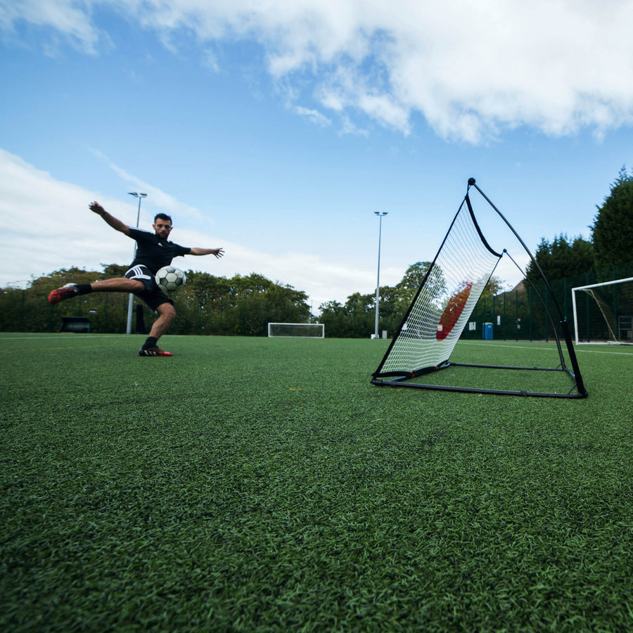 Spieler schießt einen Volley auf den SPOT Fußball-Rebounder 150 x 100 cm auf einem Kunstrasenplatz, als Weitwinkelaufnahme aus niedriger Perspektive.