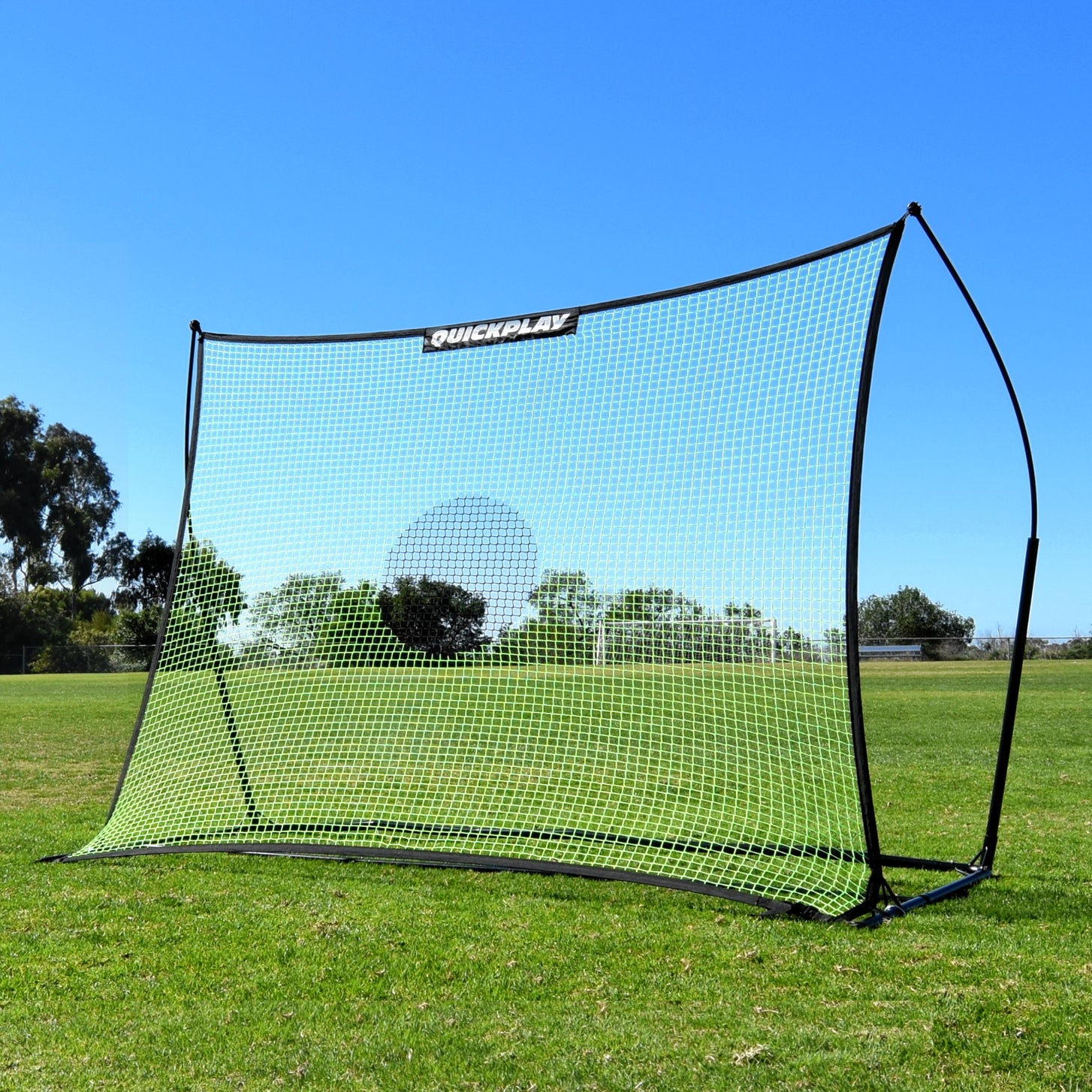 TEKKERS Net XL Fußball-Rebounder 240 x 180 cm auf Rasen unter blauem Himmel, schräg von vorn gesehen.
